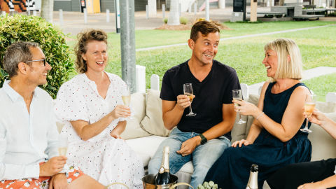 4 people sitting together talking and smiling with champagne in their hands, and a cheese board on the table in front of them